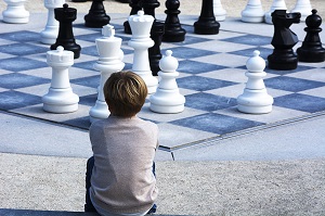 zdjęcie chłopca , ujęcie od tyłu. przed chłopcem duże figury, szachy poustawiane na szachowicy