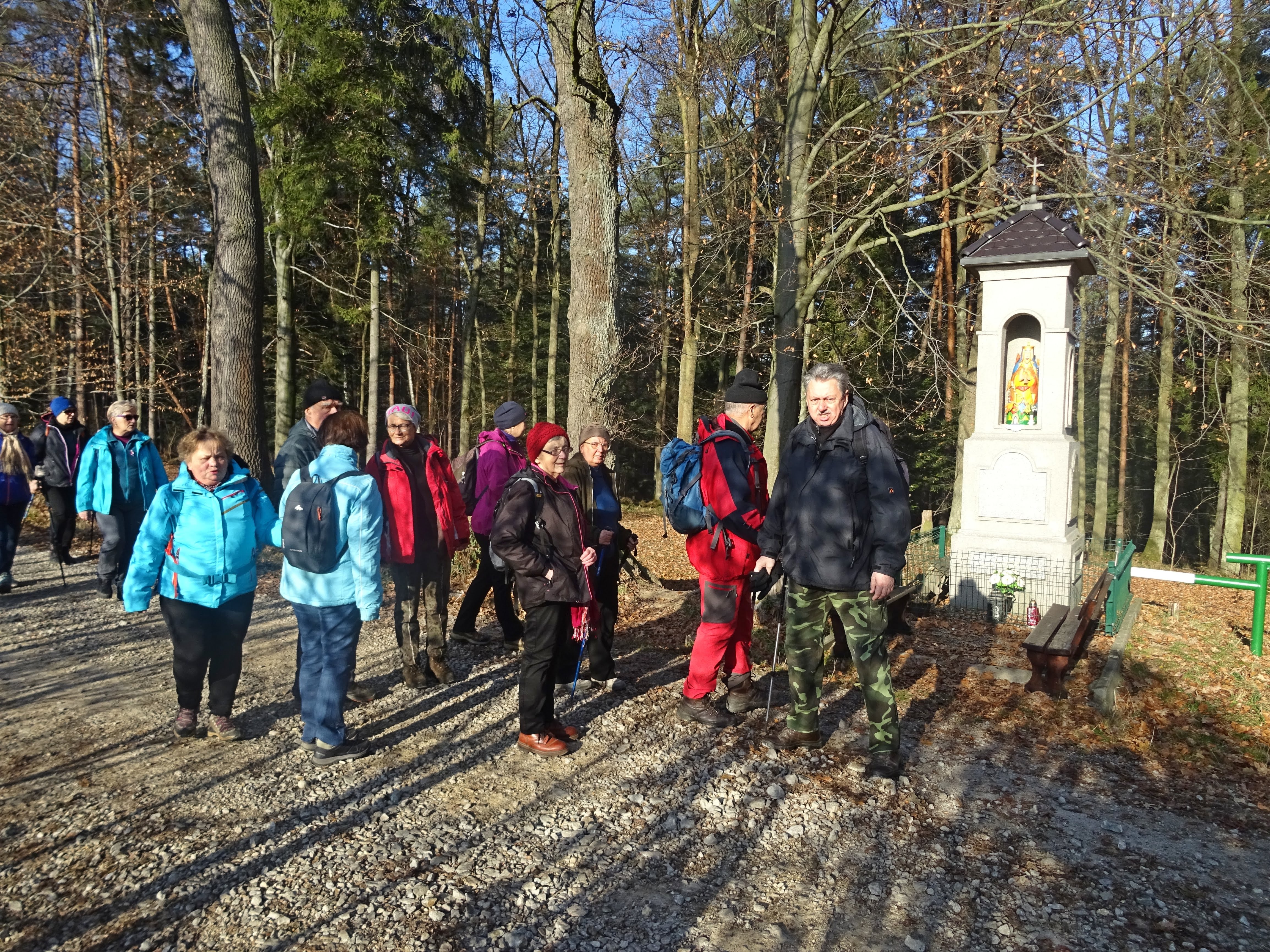 grupa osób w lesie stająca przy kapliczce.